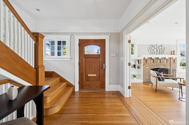 foyer entrance featuring stairs, a brick fireplace, wood finished floors, and baseboards