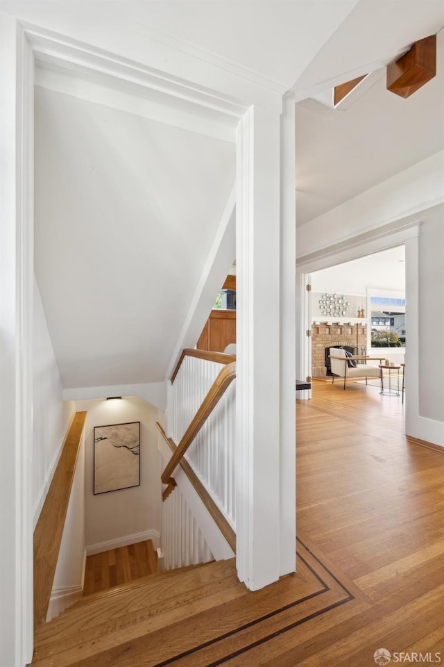 staircase featuring lofted ceiling, a fireplace, and wood finished floors