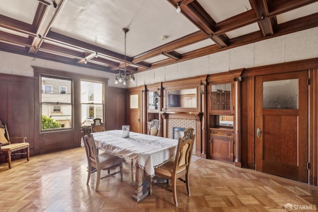 dining room featuring beam ceiling, a notable chandelier, a tiled fireplace, wood walls, and coffered ceiling