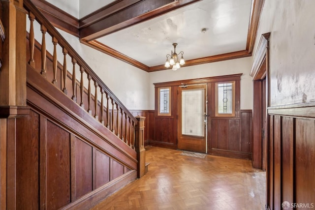 foyer with wooden walls, a notable chandelier, stairway, wainscoting, and crown molding