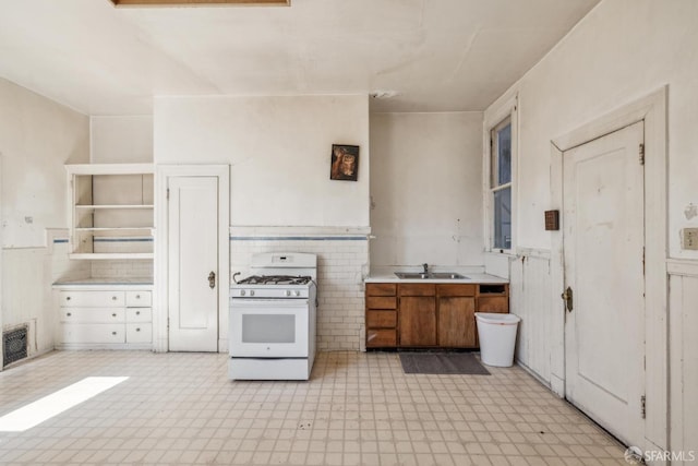 kitchen with a wainscoted wall, a sink, visible vents, white range with gas cooktop, and light floors