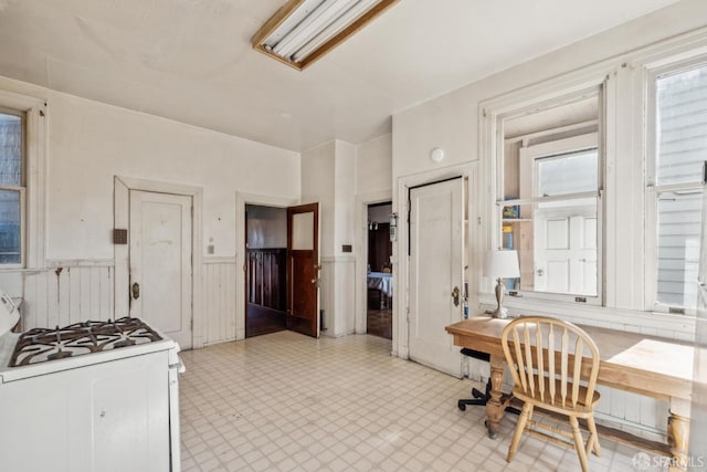 kitchen featuring a wainscoted wall, white gas stove, and light floors