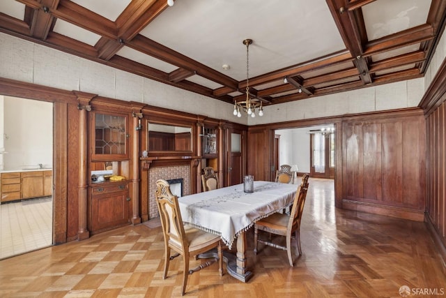 dining area featuring a chandelier, wooden walls, coffered ceiling, beam ceiling, and a tiled fireplace