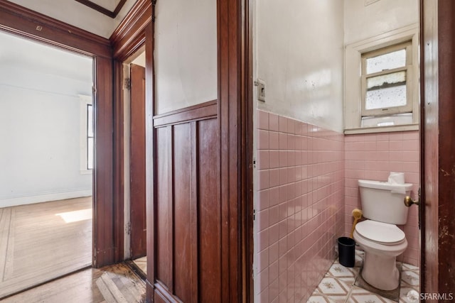 bathroom with a wainscoted wall, plenty of natural light, toilet, and tile walls