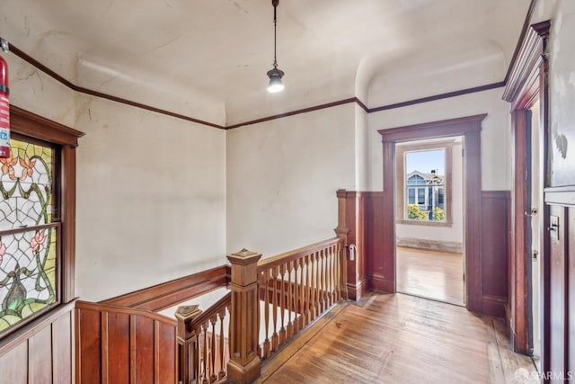 corridor featuring ornamental molding, light wood-style flooring, wainscoting, and an upstairs landing