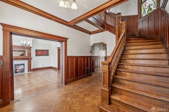 stairway featuring a wainscoted wall, wooden walls, a fireplace with flush hearth, and a notable chandelier