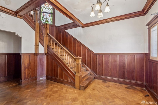 staircase with a wainscoted wall, a wealth of natural light, and an inviting chandelier