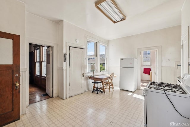 kitchen featuring white appliances, light floors, and a wainscoted wall