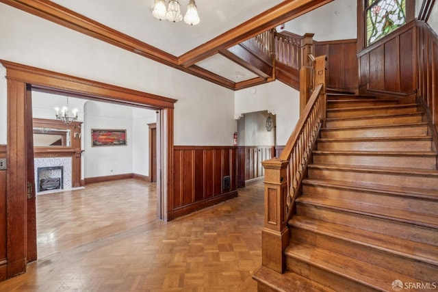 stairway featuring an inviting chandelier, a fireplace with flush hearth, wooden walls, and wainscoting