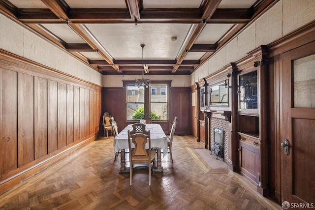 unfurnished dining area featuring beam ceiling, a notable chandelier, a fireplace with flush hearth, wood walls, and coffered ceiling