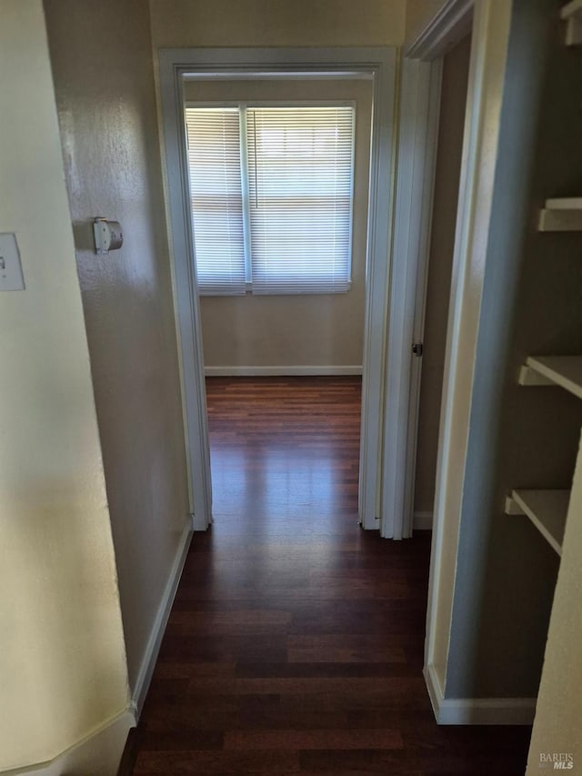 corridor featuring baseboards and dark wood finished floors