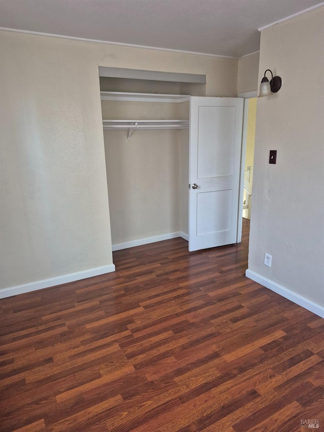 unfurnished bedroom with baseboards, a closet, crown molding, and wood finished floors