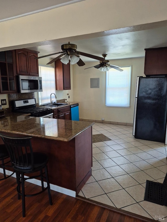 kitchen with a sink, a peninsula, stainless steel appliances, dark stone countertops, and a breakfast bar area