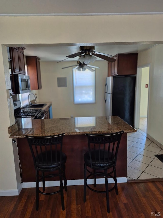 kitchen featuring a ceiling fan, baseboards, a kitchen breakfast bar, a peninsula, and appliances with stainless steel finishes