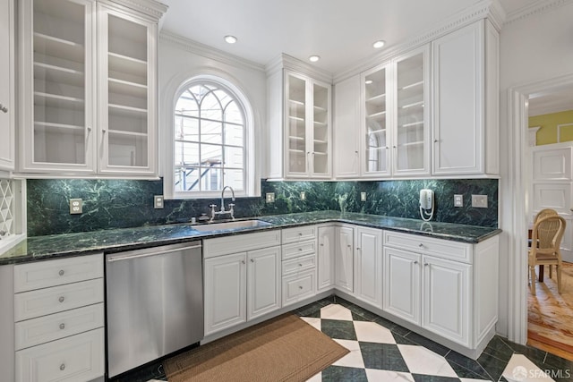 kitchen with stainless steel dishwasher, ornamental molding, white cabinetry, dark stone countertops, and a sink