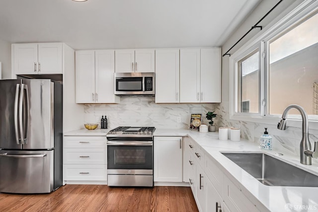kitchen featuring stainless steel appliances, a sink, backsplash, and white cabinets