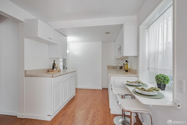 kitchen with light wood-style floors, light countertops, white cabinetry, and baseboards