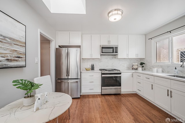 kitchen featuring stainless steel appliances, a sink, backsplash, light wood-style flooring, and white cabinets