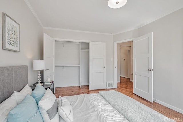 bedroom with a closet, crown molding, wood finished floors, and baseboards