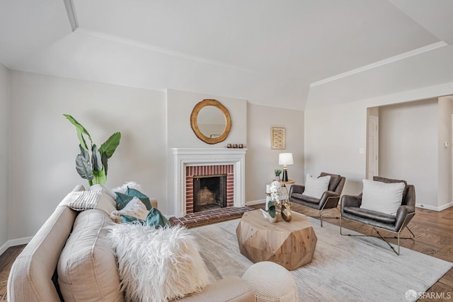 living area featuring baseboards, wood finished floors, a brick fireplace, and ornamental molding