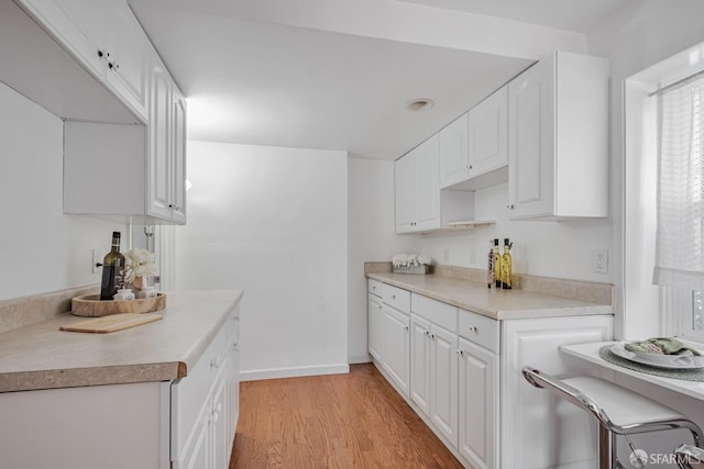 kitchen with light wood finished floors, white cabinetry, light countertops, and baseboards