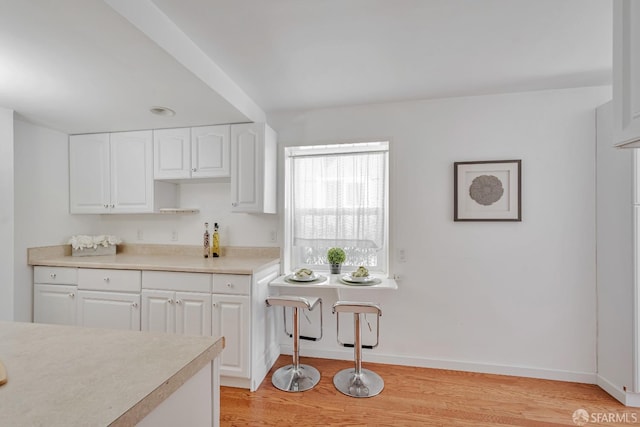 kitchen with light wood-type flooring, white cabinets, light countertops, and baseboards