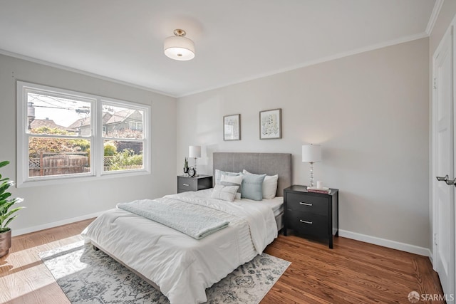 bedroom with ornamental molding, baseboards, and wood finished floors