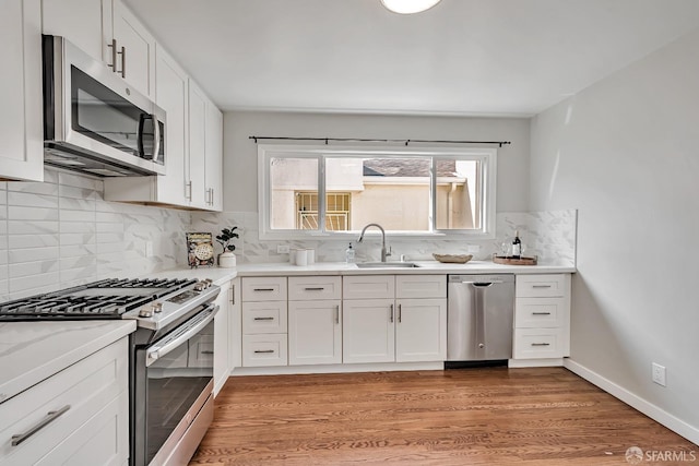 kitchen featuring appliances with stainless steel finishes, light wood-style floors, white cabinets, a sink, and tasteful backsplash