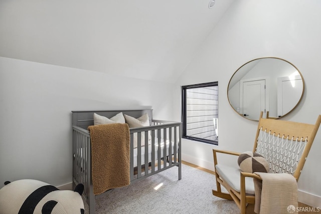 bedroom featuring light carpet, lofted ceiling, and a nursery area