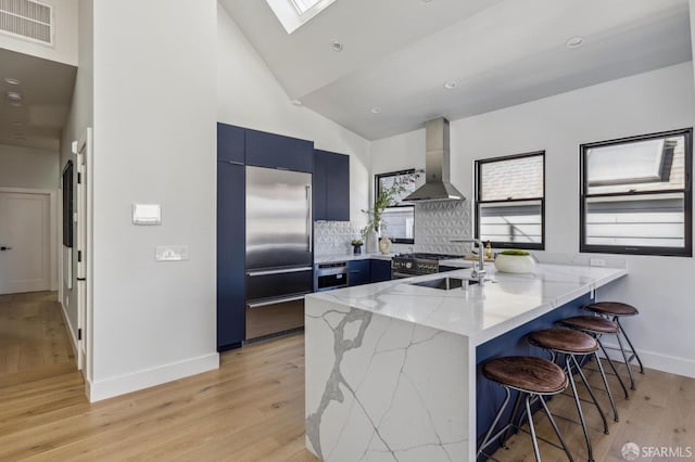 kitchen with wall chimney exhaust hood, high end appliances, sink, kitchen peninsula, and a breakfast bar