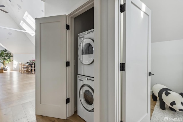 laundry area with a skylight, stacked washing maching and dryer, and light wood-type flooring