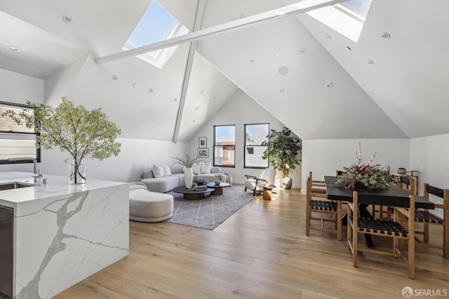 living room featuring sink, light hardwood / wood-style flooring, and lofted ceiling with skylight