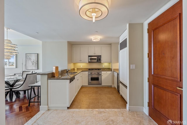 kitchen with a peninsula, dark stone counters, a sink, stainless steel appliances, and white cabinetry