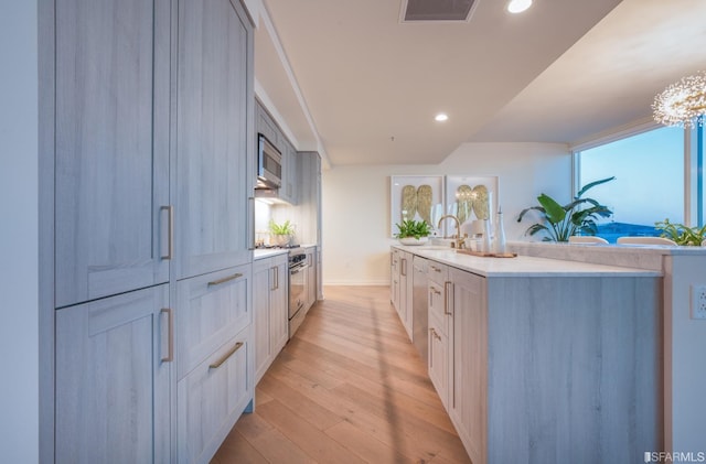 kitchen with sink, stainless steel appliances, a chandelier, and light wood-type flooring