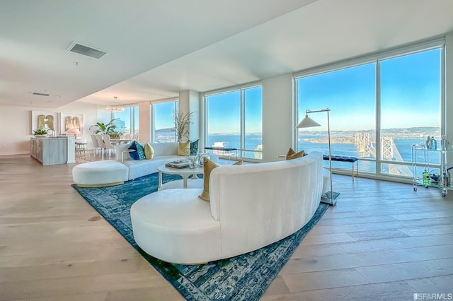 living room featuring floor to ceiling windows, a water view, a chandelier, and light wood-type flooring