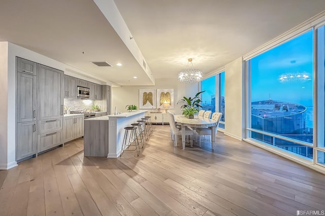 kitchen featuring a kitchen island with sink, a breakfast bar area, stainless steel appliances, pendant lighting, and gray cabinets