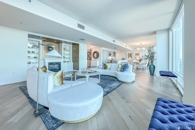 living room with built in features, light hardwood / wood-style flooring, and an inviting chandelier