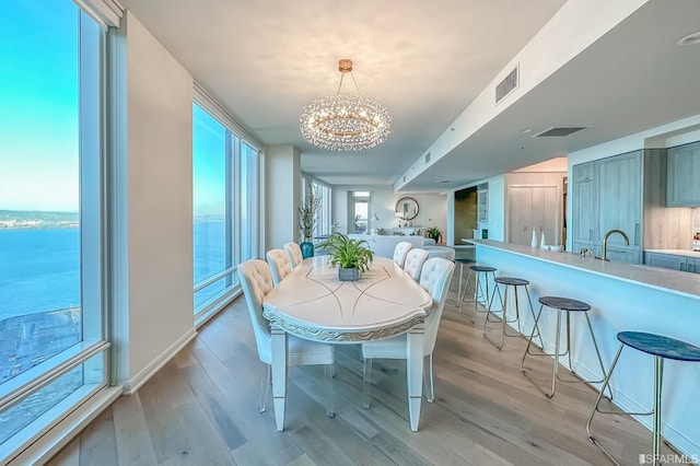 dining area featuring light hardwood / wood-style floors, a notable chandelier, and a water view