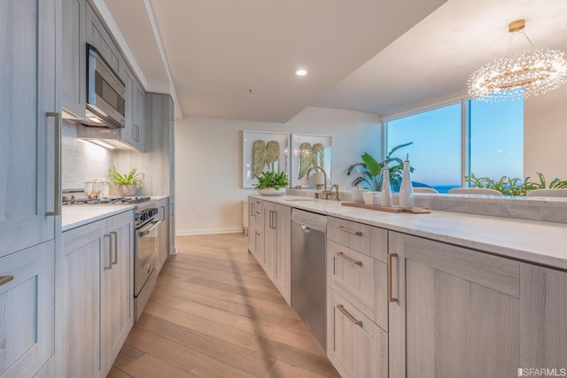 kitchen featuring stainless steel appliances, sink, pendant lighting, a chandelier, and light hardwood / wood-style floors