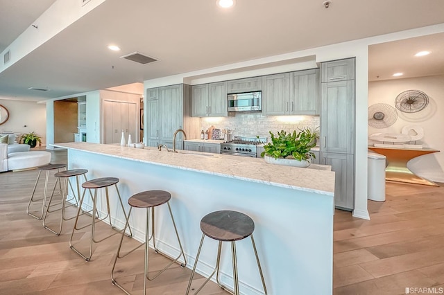 kitchen with decorative backsplash, stainless steel appliances, a kitchen bar, light wood-type flooring, and light stone counters