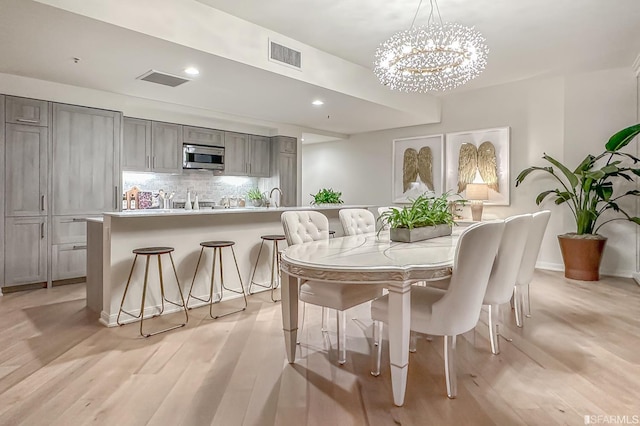 dining space with an inviting chandelier, sink, and light hardwood / wood-style floors