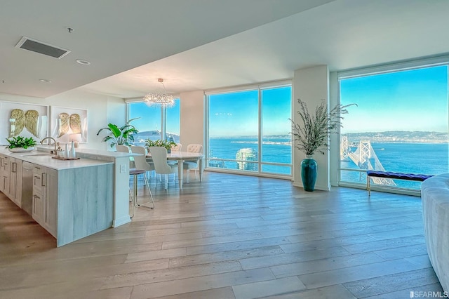 kitchen with hanging light fixtures, an inviting chandelier, light hardwood / wood-style floors, sink, and a water view