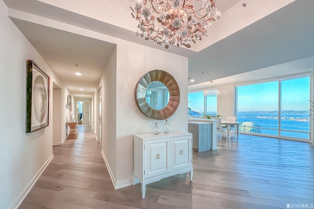 hall with a notable chandelier, a water view, and light hardwood / wood-style floors