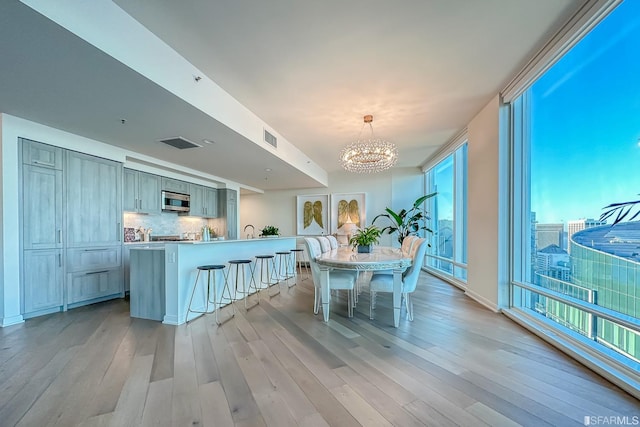 kitchen featuring gray cabinetry, decorative light fixtures, decorative backsplash, light hardwood / wood-style flooring, and an inviting chandelier