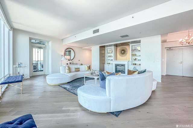 living room with light hardwood / wood-style floors, a notable chandelier, and built in shelves