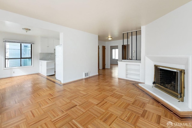 unfurnished living room with a fireplace with raised hearth, visible vents, and baseboards