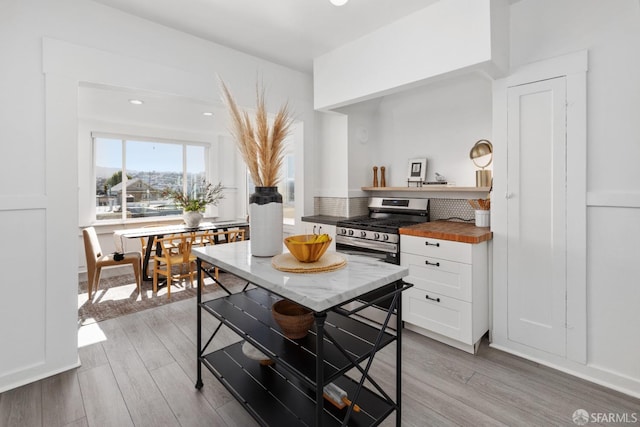 kitchen with stainless steel gas range oven, light wood-type flooring, white cabinetry, wood counters, and open shelves