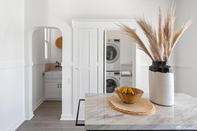 laundry room with wood finished floors, baseboards, laundry area, a sink, and stacked washer and clothes dryer