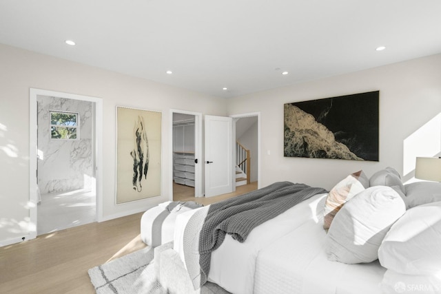 bedroom featuring wood finished floors, recessed lighting, a walk in closet, ensuite bathroom, and baseboards
