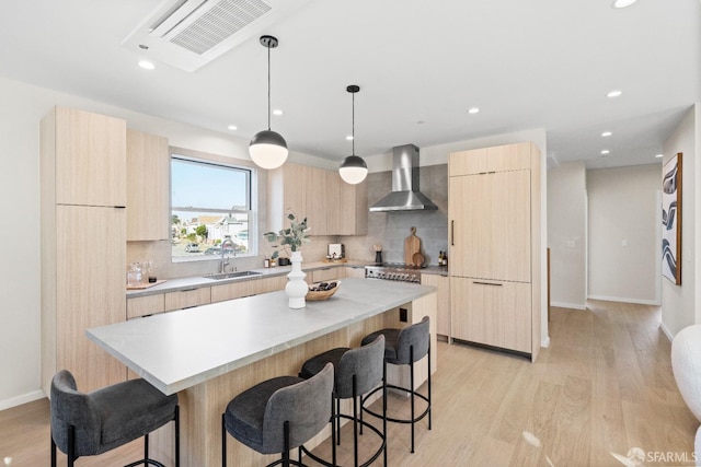 kitchen featuring wall chimney exhaust hood, light brown cabinets, modern cabinets, and recessed lighting